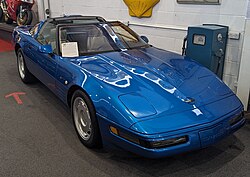 A bright beetle-blue or brilliant lake-blue sports car with a partially removable top is parked indoors. It is highly polished as if it's well taken care of.