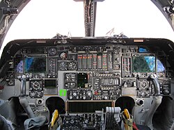A flightdeck, dominated by a mix of new and analogue instruments. On both sides are control yokes. Light enters through the forward windows