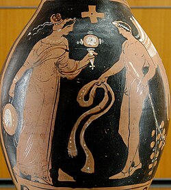 Woman holding a mirror and a tambourine facing a winged genie with a ribbon and a branch with leaves. Ancient Greek red-figure oinochoe, c. 320 BC, from Magna Graecia. (Notice the coloured decorative woven stripes hanging on the tambourine, which can still be seen today on the tamburello, the tambourine of Southern Italy.)