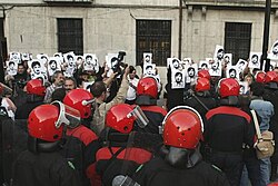 Demonstrators holding pictures in front of uniformed people in red helmets, perhaps police officers