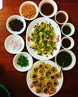 Plates of panipuri and another chaat, surrounded by filling ingredients and five sauces