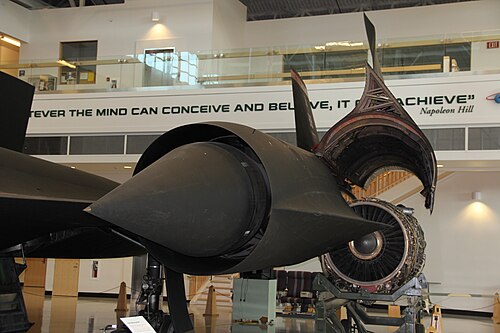A view of the entry to an SR71 Mach 3.2 mixed external-internal inlet looking in direction of airflow to the engine. The centre translating cone has 26 inches of travel between extended, up to M1.6 (shown), and fully retracted at M3.2. An oblique shock from the cone tip, an internal oblique shock from the cowl lip and a normal shock[103] give the required pressure recovery at M3.2. The boundary layers on the cone and cowl inner surface have to be removed before the final shock-wave where the flow becomes subsonic. Otherwise shock-induced separation occurs. The two removal features are just visible. The cone boundary layer is removed through the band of holes (porous bleed). The boundary layer on the cowl inner surface is removed through a shock-trap[104] bleed. This ram bleed is just visible on the lower surface in front of a row of streamlined lumps called "mice" which reduce the rate of diffusion.[105]