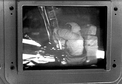 Black and white still image of a screen showing an astronaut descending the moon lander ladder