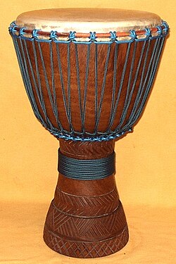 Brown goblet-shaped wood and leather drum with blue rope on an alabaster background