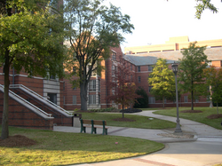 A red brick and white concrete, four-story apartment building with a landscaped courtyard in the foreground