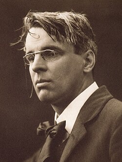 A posed black and white photograph of Yeats. He is wearing smart clothes and spectacles, while his hair looks a bit tousled