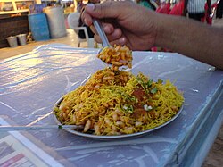 Bhel puri being eaten with a spoon on an outdoor table.