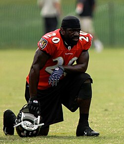 Ed Reed in a Baltimore Ravens jersey resting on one knee with his helmet on the ground in his hand.