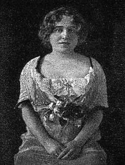 Portrait of a seated young woman with her arms clasped in her lap.