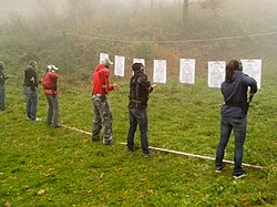 A line of people in front of targets reaching for their guns in holsters.