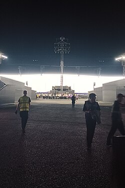Men walk in front of a white screen in a stadium