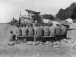 Apprentices of No. 1 School of Technical Training listen to a lecture on servicing aircraft in the field, in front of a line of instructional airframes, during the early 1940s.