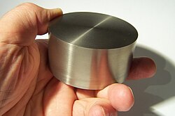 A hand holding a cylinder of reflective silvery metal