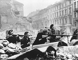 Black-and-white photograph of Polish resistance fighters in an urban setting with rubble and smoke, one carrying a wz. 28 light machine gun.