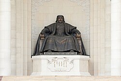A statue of a seated man, placed on an inscribed plinth.