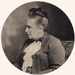 Black and white of a seated older woman in profile, her hair up, in a formal dark suit with a lace cloth at the neck
