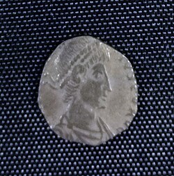 A small silver coin mostly consisting of a human head and shoulders. The shape is irregular and there is only a vestige of writing.