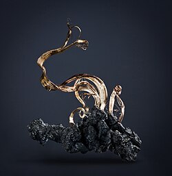 A cluster of bright silver, wire-like, and crystalline metallic mineral protruding from a dark, grayish-black matrix.