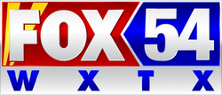 The Fox network logo in silver on a red swallowtail holding shape with two yellow searchlights beneath the F. The remainder of the box area is filled by a blue shape with a silver numeral 54. Beneath, in blue on a silver frame, is the call sign W X T X.