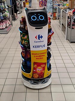 A robot with a catlike face, laden with bags of chips in the middle of a supermarket.