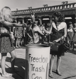 Two women toss items into the Freedom Trash Can while a female reporter looks on.