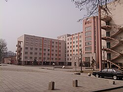 A large square with a fountain in the middle sits before several buildings with a pink rendering. The buildings are used for teaching as part of Anshan Normal University.
