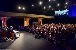 Image shows a panel onstage facing an audience in an auditorium.