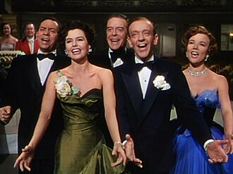 five performers singing together, smiling