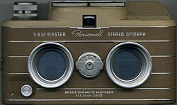 A view master camera from the front, showing the twin lenses and brown color of the body. The viewfinder is visible above the lenses, and a small dial to select between "A" and "B" settings is visible between the lenses.