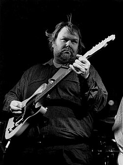A black-and-white photograph of musician Al Anderson playing an electric guitar