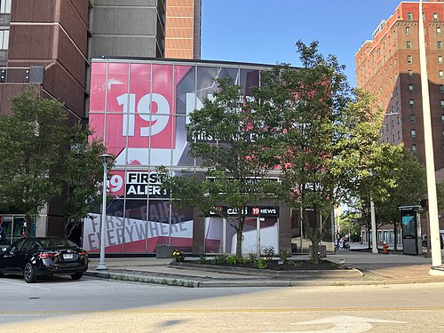 Exterior of the southern portion of Reserve Square, consisting of a three-story section including a lower level. The ground level entrance sign reads "WOIO-TV - WUAB-TV RAYCOM MEDIA STATIONS" with logos for "CBS 19", "19 ACTION NEWS" and "MY 43". A full size ad, "19 Action News: Honest, Fair, Everywhere" is at the corner of the building.
