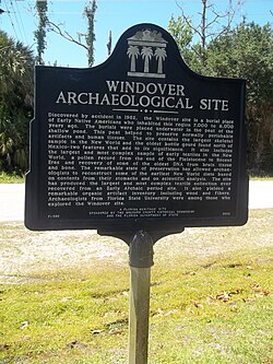 A green sign displaying the words "Windover Archaeological Site" is shown in front of a green lawn with a blue sky