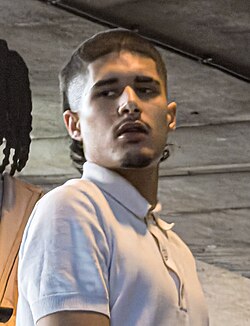 A photo of British rapper Fakemink performing on stage. He has a unique hairstyle with a mullet in the back and a fade on the sides.
