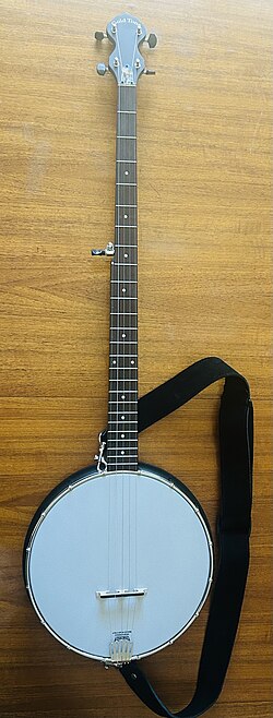 An banjo lying flat on a table. It has a longer neck than a usual banjo, and three extra frets. It is open-backed.