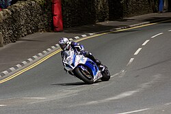 Blue and white racing motorcycle with rider slowing downhill when approaching a right hand bend