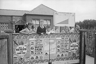 Children of Blean Village School, Whitstable Road, near Canterbury in Kent lean on the school fence to show their support for the National Savings Scheme. Posters advertising the scheme and a graph showing the school's saving progress can be clearly seen.