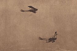 Two biplanes flying, with Ormer Locklear standing on the top wing of the lower airplane