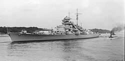Black and white photograph of the port side of a Bismarck class battleship in a body of water.