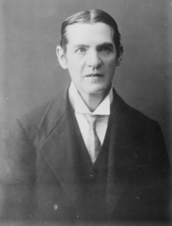A black and white portrait of a formally dressed person with neatly combed hair and a serious expression.