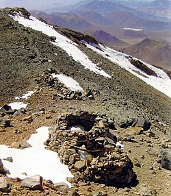 Squat ruined buildings on a mountain slope with snowy patches