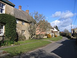 A line of cottages, some thatched, along a road.