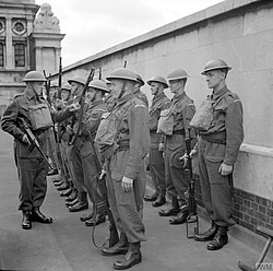 Black-and-white photograph of British Home Guard soldiers standing in formation against a wall; the soldier at the end of the front rank holds a Browning Automatic Rifle.
