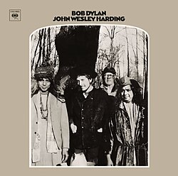 A black-and-white photo of several men standing in a wooded field, with Dylan in the center