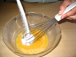 Bowl with eggs. White sugar is being poured in.