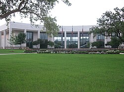 A two-story, white building in the shape of a crescent overlooks flowers and a grassy lawn