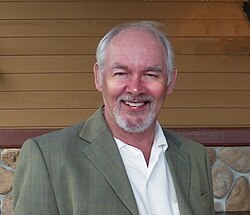 A medium, head and shoulder shot of a smiling white-haired Caucasian male with goatee and sports jacket on.