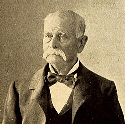 Head shot of an older man with white hair and moustache, dressed in tuxedo and bow tie.