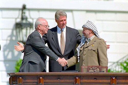 Israeli Prime Minister Yitzhak Rabin and Yasser Arafat making a historic handshake at the Oslo Accords signing ceremony on 13 September 1993 with U.S. President Bill Clinton looking on.