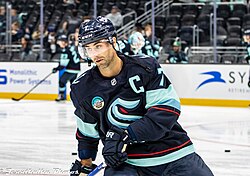 Ice hockey player holding a stick and wearing a helmet, featuring a letter C on the top right