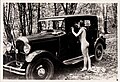 A nude woman leaning against a car